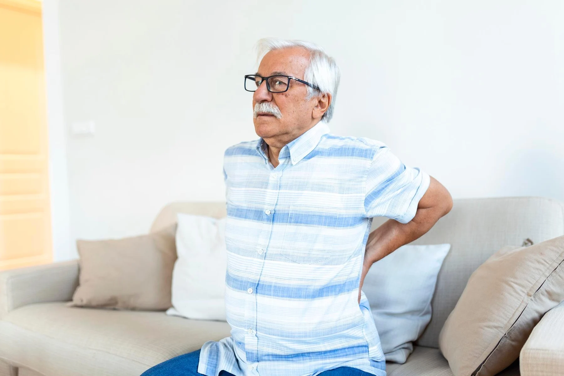 Man standing beside a sofa with a hand on his lower back